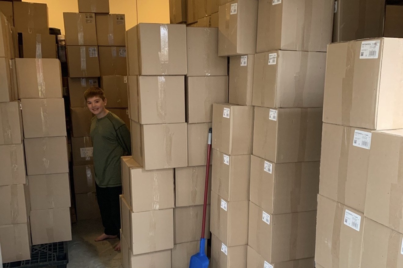 Coby standing inside a garage packed wall-to-wall with shipping cartons.