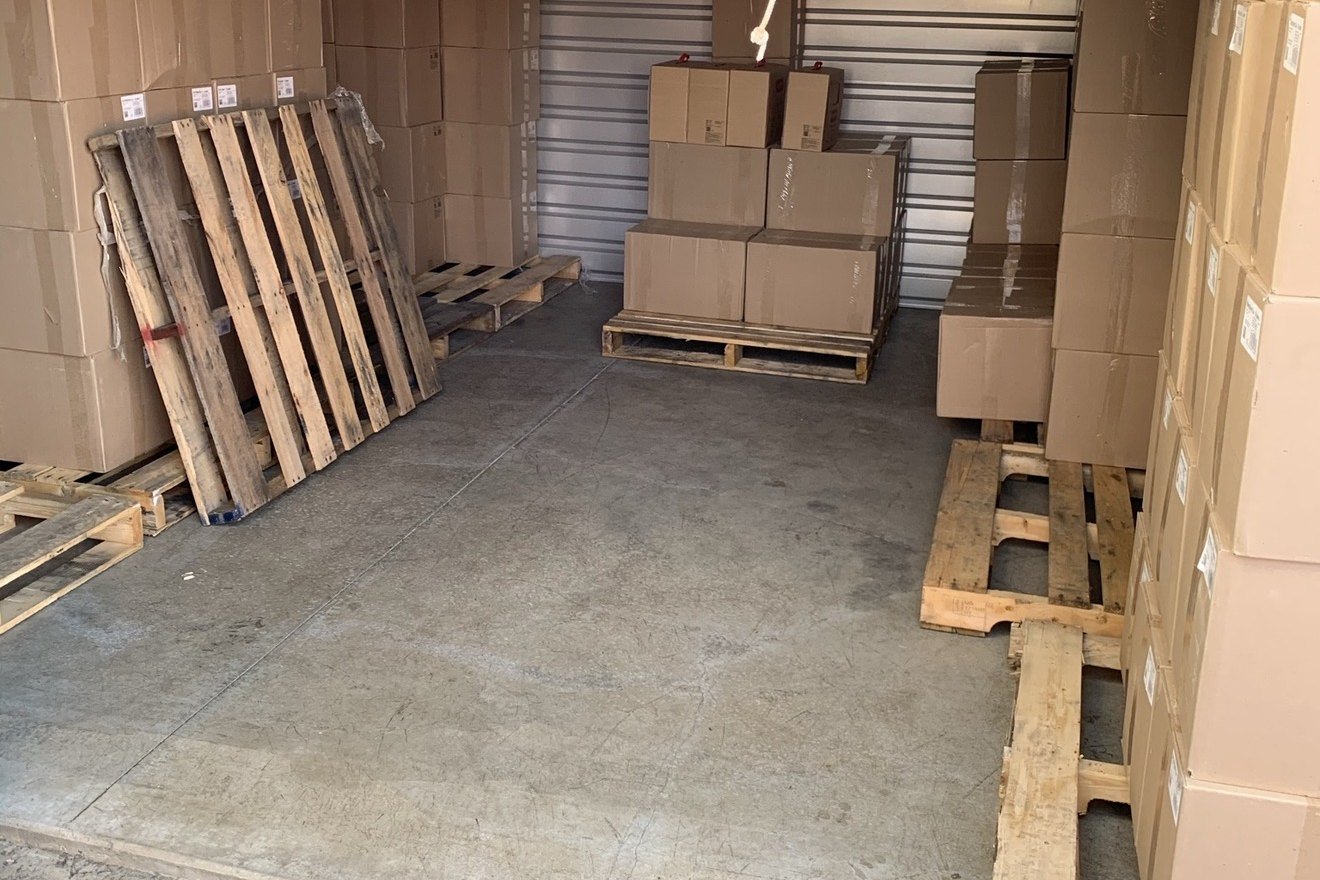 A partly emptied storage unit with cartons remaining along the walls and on pallets.