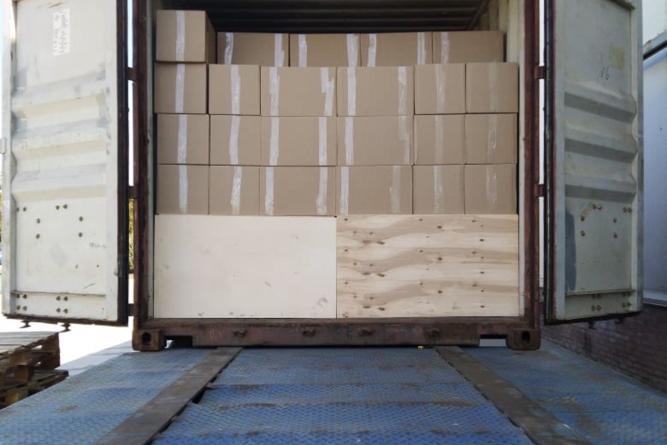 Open freight container with rows of cartons stacked above plywood bracing.